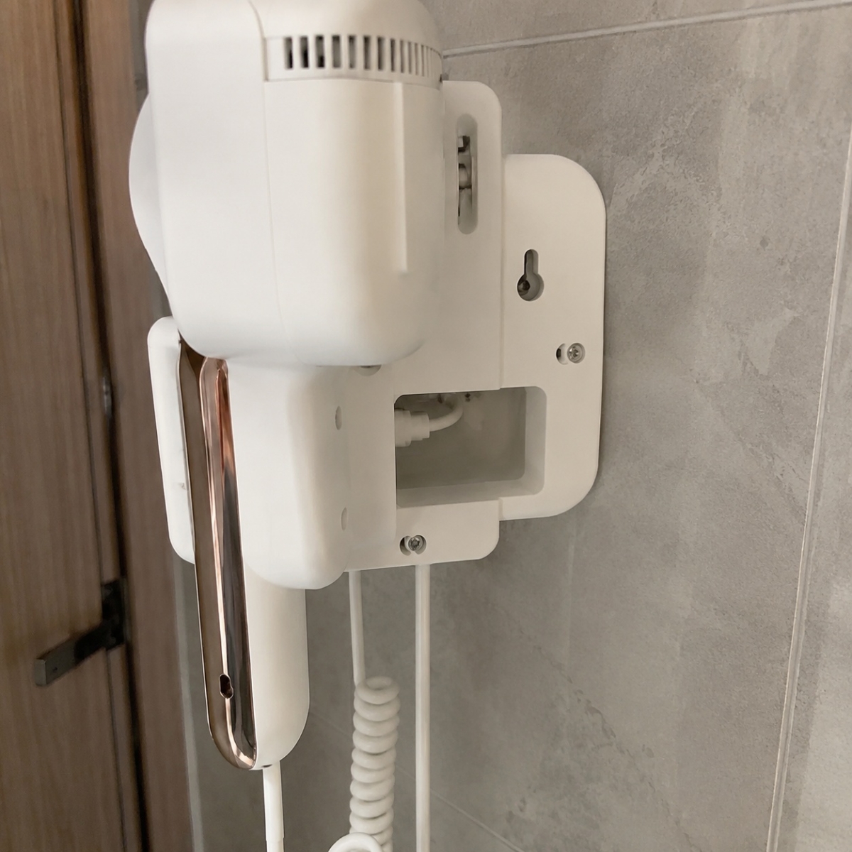 White wall-mounted hair dryer installed beside a bathroom mirror