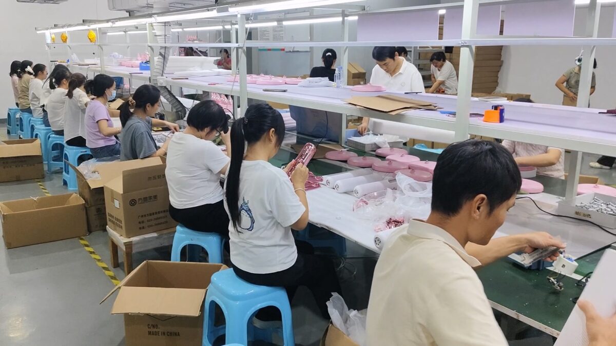 Workers assembling pink and white hair dryers on a production line